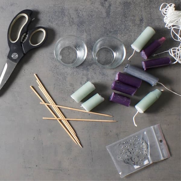 Une collection créative de matériel de bricolage, comprenant des bougies, des mèches, des supports en verre et des ciseaux, est exposée comme s'il s'agissait d'un DIY‑kaarsenproject met IKEA‑benodigdheden betreft.
