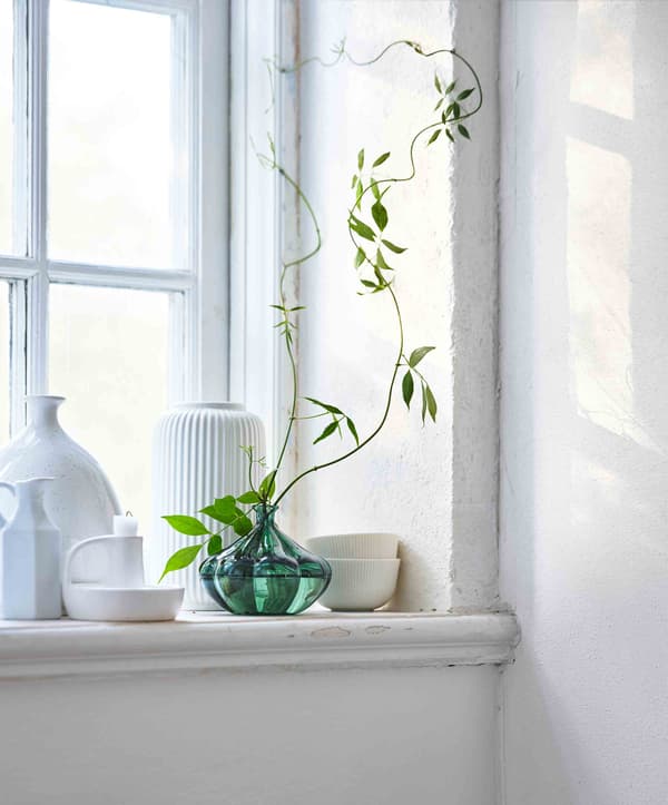 Une collection de pots en céramique blancs sur un appui de fenêtre avec un vase vert en verre au centre.