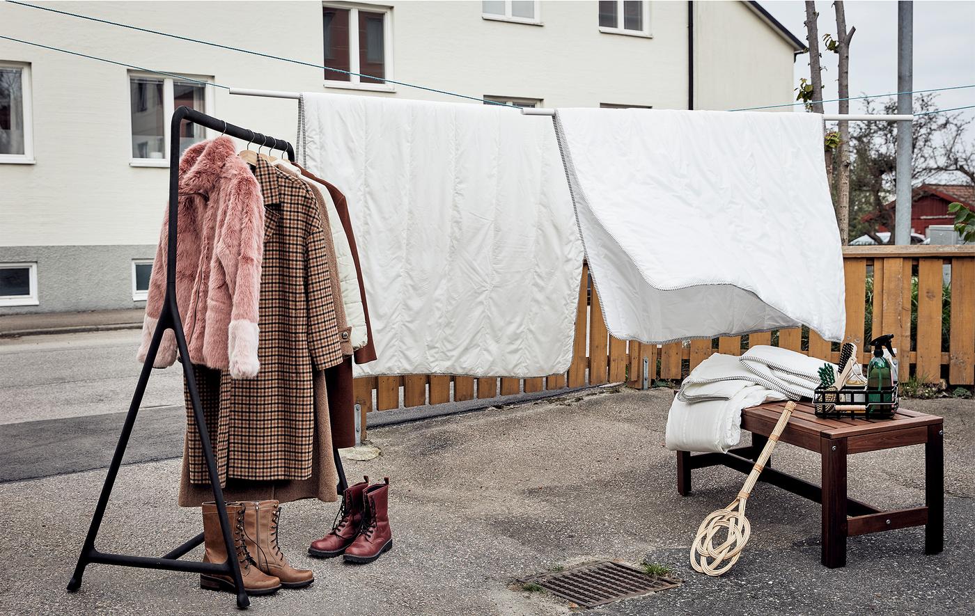 Une cour aménagée pour le nettoyage du printemps: des couettes suspendues à des cordes à linge, une tringle à vêtements, des chaussures, des textiles et des accessoires de nettoyage.
