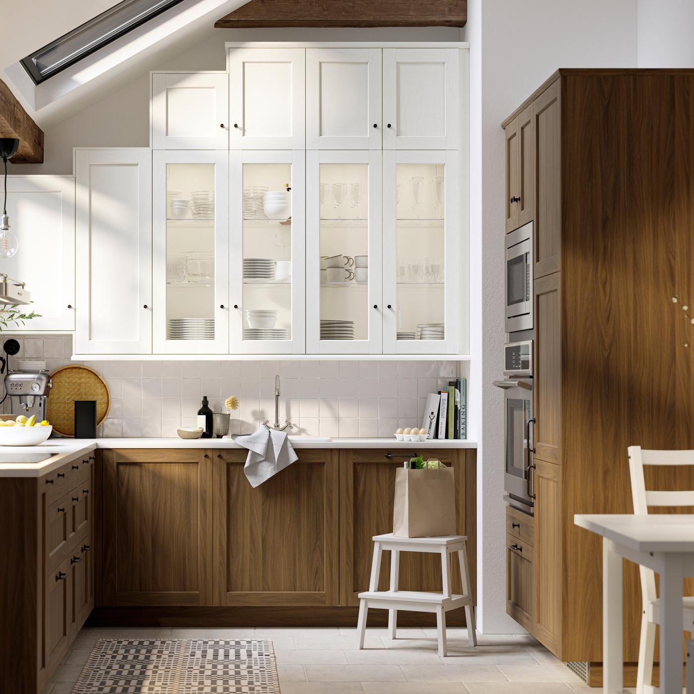 Une cuisine avec des portes ENKÖPING blanches à effet bois et des portes vitrées, ainsi que des portes et des façades de tiroirs ENKÖPING brunes à effet noyer.