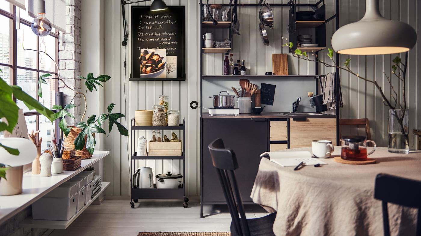 Une cuisine avec une kitchenette ÄSPINGE, une desserte NISSAFORS noire contenant divers objets, une table de cuisine et des chaises.