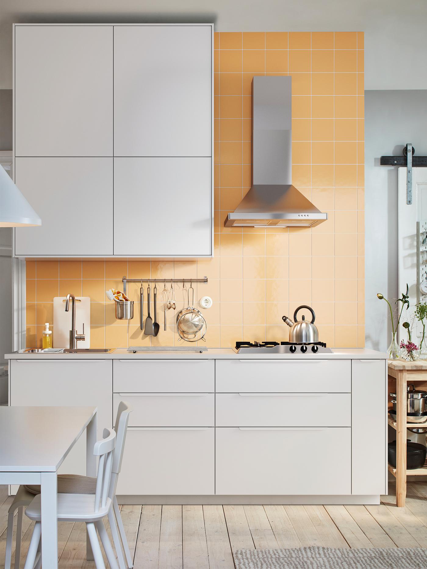 Une cuisine blanche avec des armoires blanches, une hotte murale en inox ainsi qu’une table et des chaises blanches.
