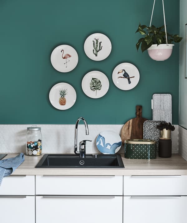 Une cuisine blanche dotée de plans de travail en bois et un mur vert avec des assiettes décoratives.