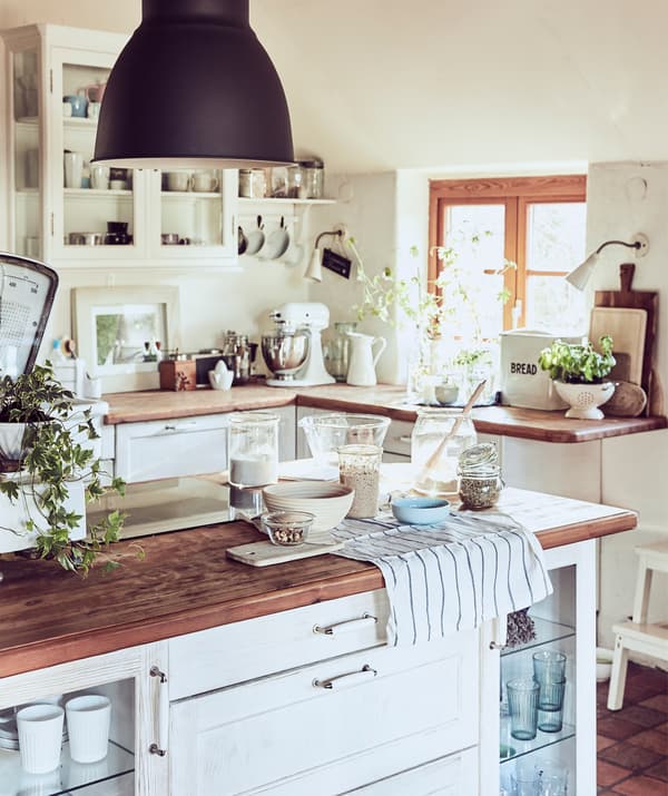 Une cuisine blanche et rustique avec des plans de travail en bois, des accessoires de pâtisserie et un îlot de cuisine.