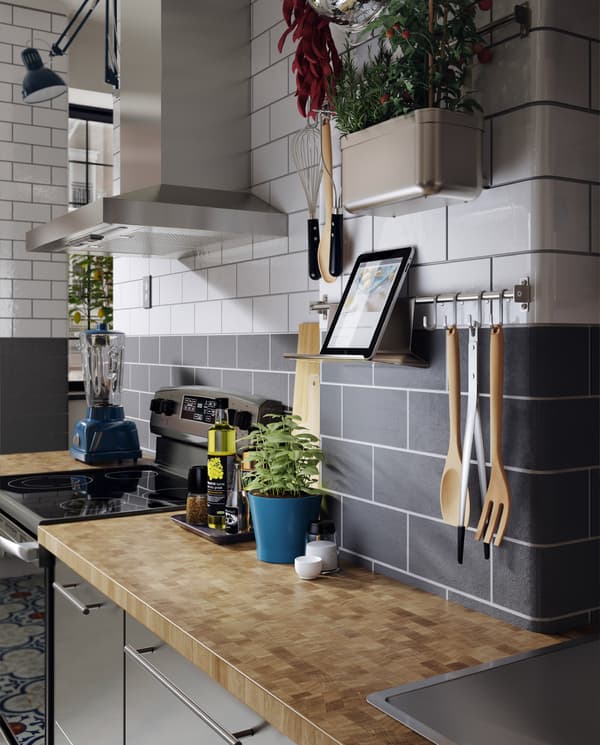 Une cuisine en acier inoxydable, un plan de travail en bois, des fines herbes fraîches et un rail mural avec une tablette sur un support pour tablette.