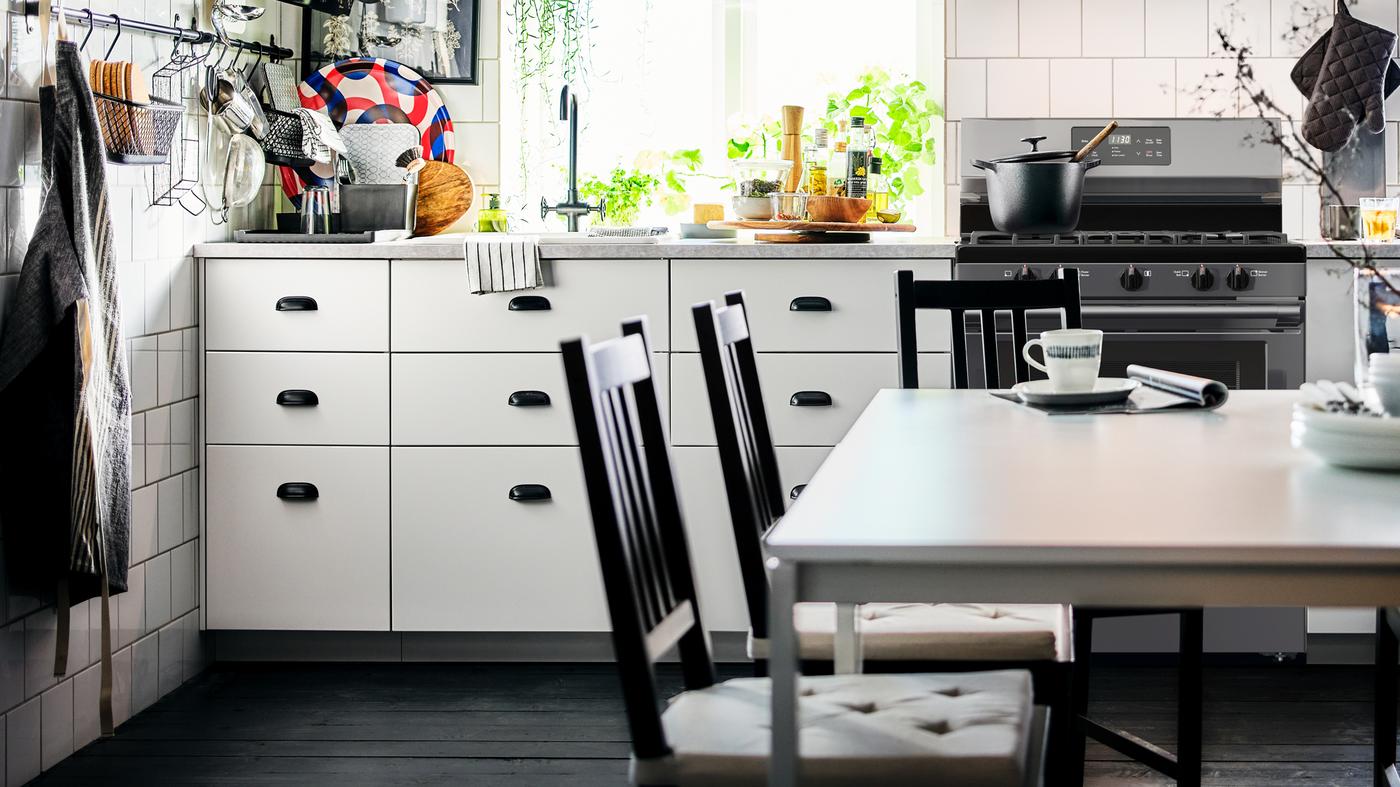 Une cuisine en noir et blanc avec des armoires inférieures blanches et une salle à manger centrée sur deux tables MELLTORP blanches.