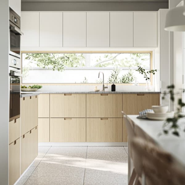 Une cuisine IKEA en L avec des éléments hauts et bas blancs et des façades aspect bois avec poignée intégrée du système de cuisine METOD