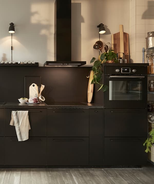 Une cuisine noire équipée d’une hotte aspirante, d’un four encastré et de plans de travail foncés.
