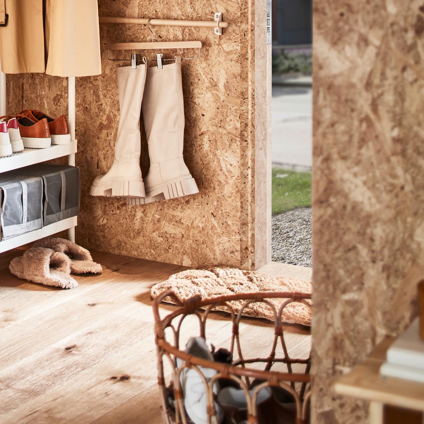 Une entrée avec un rangement ouvert pour vêtements et chaussures, un panier en rotin contenant des chaussures et une barre supportant des bottes sur un porte-jupe.