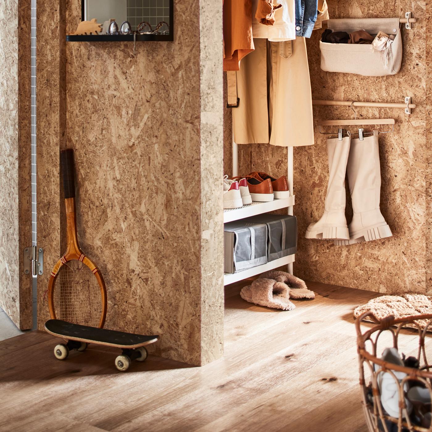 Une entrée avec un rangement ouvert pour vêtements et chaussures, un panier en rotin contenant des chaussures et une barre supportant des bottes sur un porte-jupe.