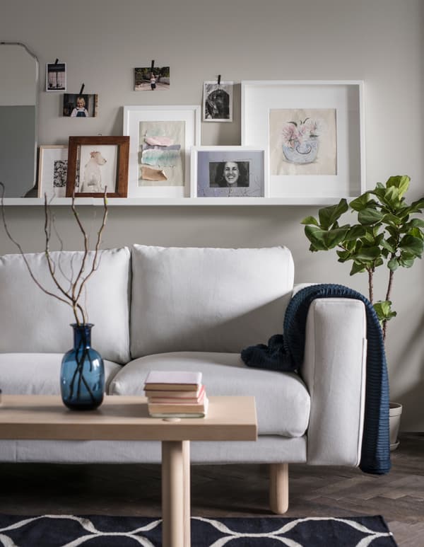 Une étagère pour photos installée au-dessus d’un canapé sert de présentoir à des photos et des tableaux tandis que de plus petites photos sont fixées au mur avec de l’adhésif décoratif.