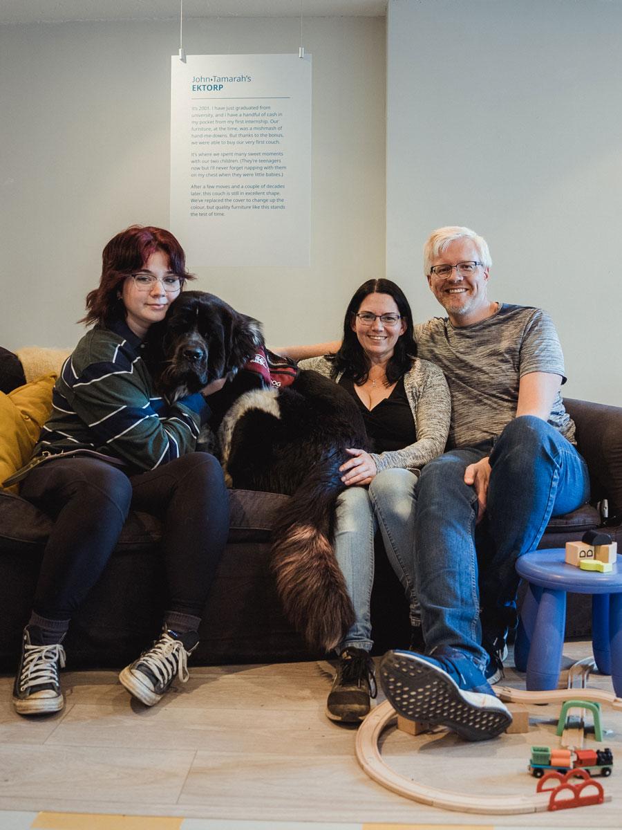 Une famille avec un chien est assise sur un canapé IKEA EKTORP. Un tabouret d’enfant et un ensemble de train sont placés près du canapé.
