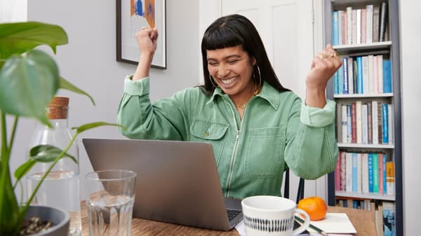 Une femme est assise devant un ordinateur portable et lève les poings d’un air ravi.