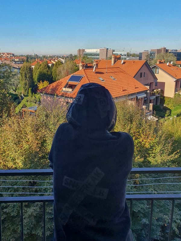 Une femme portant un chandail à capuchon debout sur un balcon en train d'observer le voisinage.