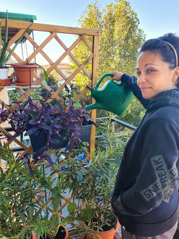 Une femme portant un chandail à capuchon noir arrose ses plantes avec un arrosoir vert.