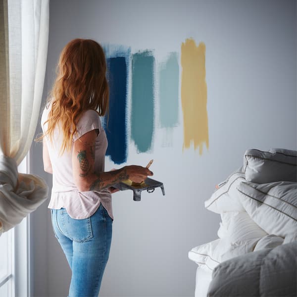 Une femme teste différentes teintes de couleurs pour sa chambre à coucher en les étalant sur le mur.