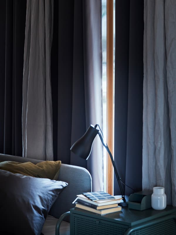 Une fenêtre dans une chambre à coucher bleue, le soleil presque entièrement caché derrière des rideaux occultants HILLEBORG.