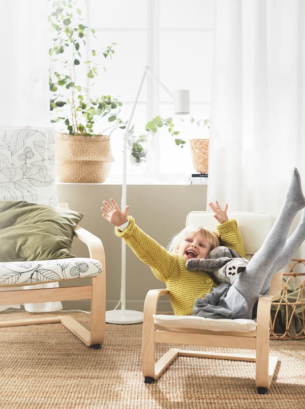 Une fillette rieuse confortablement installée avec sa peluche dans un fauteuil pour enfants JPOÄNG placé un côté d’un fauteuil de la même collection en taille adulte.
