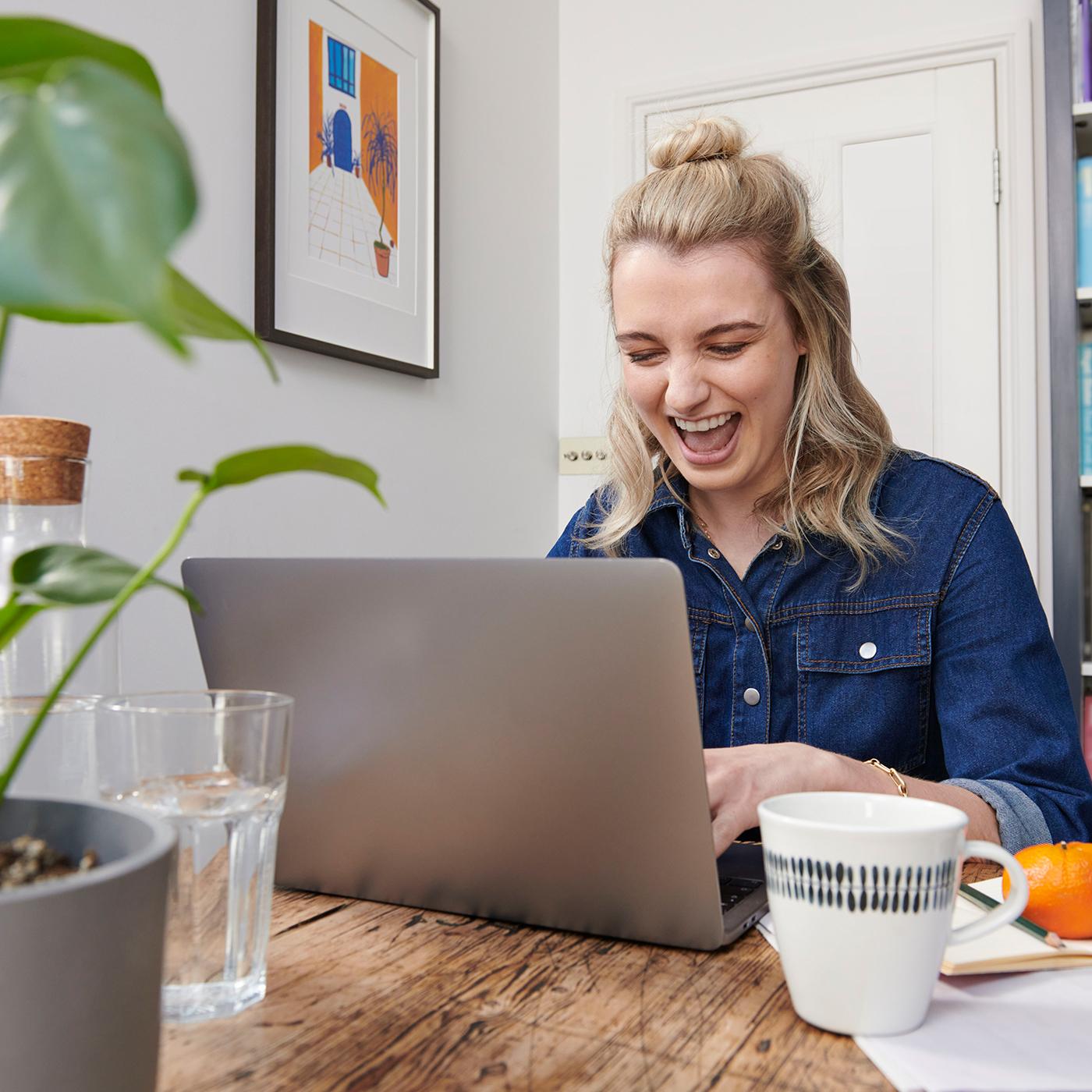 Une jeune femme sourit devant son ordinateur portable