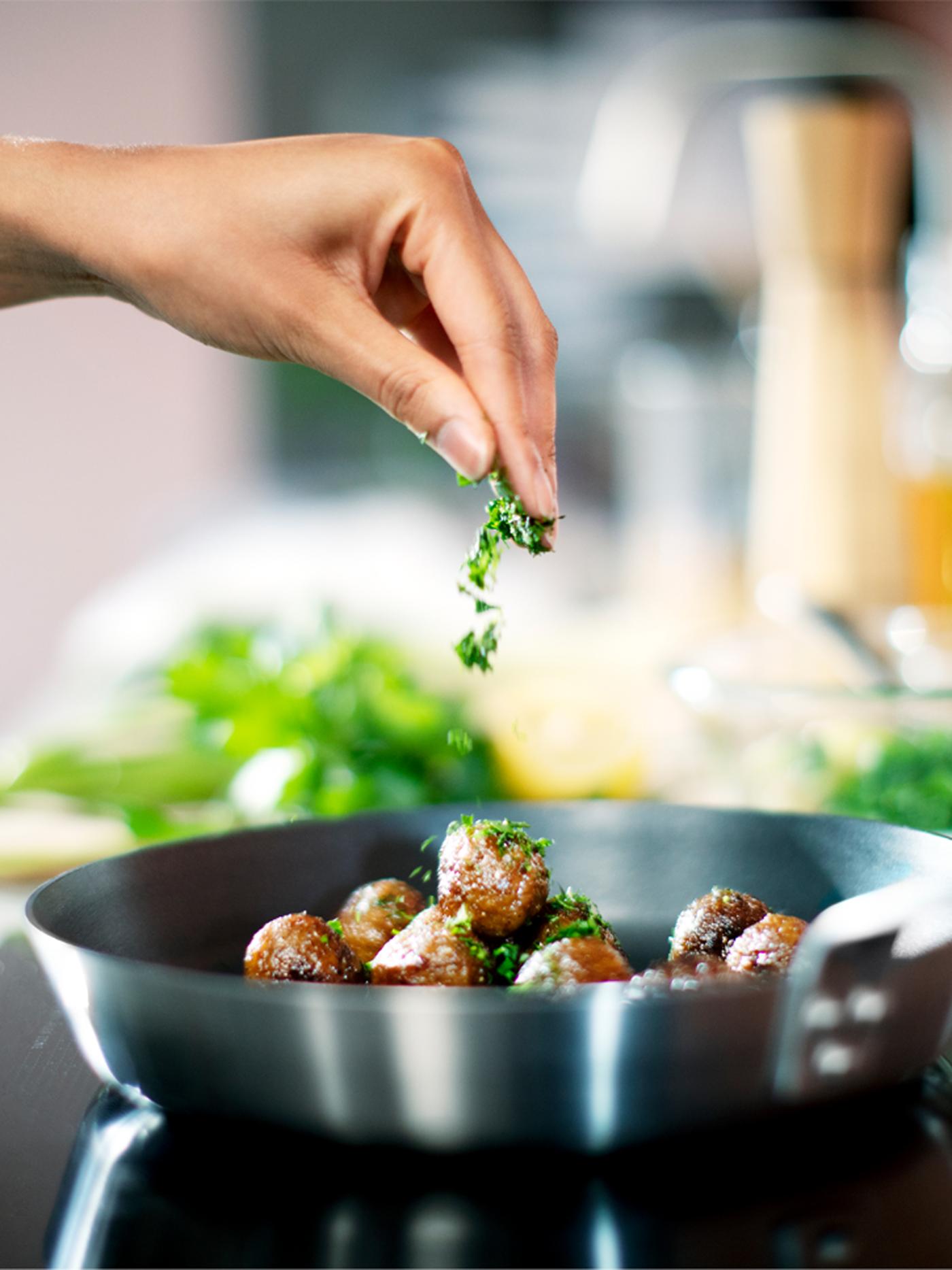 Une main assaisonne des boulettes végétales disposées dans une poêle à frire IKEA 365+.