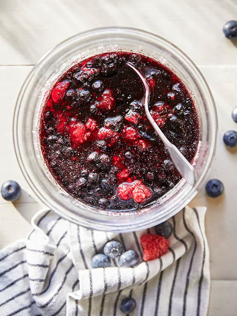 Une myrtille et une fraise reposent dans un mélange crémeux présenté dans un verre, avec une cuillère à proximité.