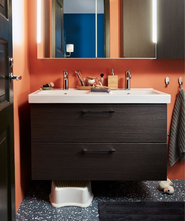 Une partie de la salle de bain: lavabo double avec tiroirs, meuble à miroir au-dessus, tabouret enfant et canard en caoutchouc en dessous.