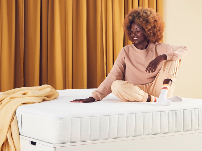 une personne assise sur un matelas, une main posée dessus.