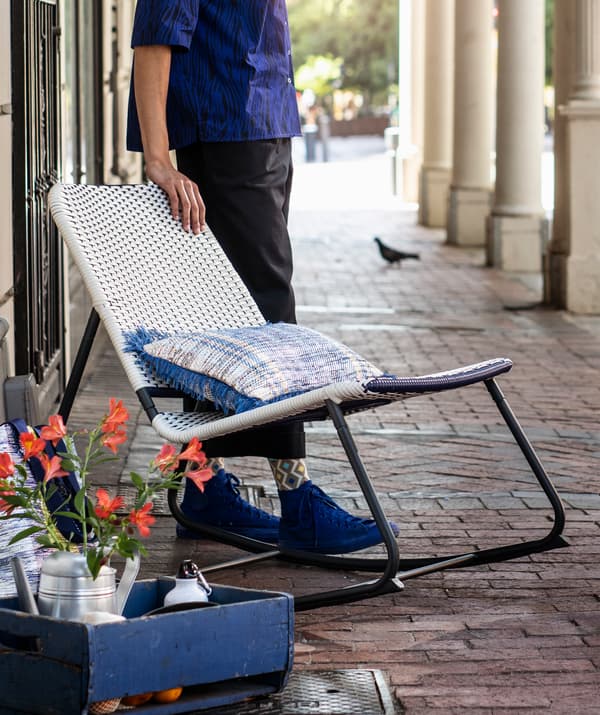 Une personne debout à côté d’un fauteuil à bascule bleu et blanc avec un cadre métallique.