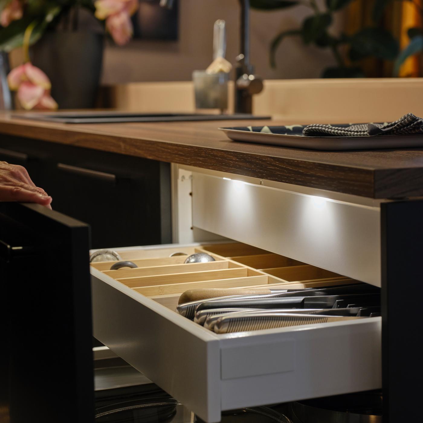 Une personne ouvre un tiroir de cuisine à façade anthracite mat, révélant de l’éclairage pour tiroir à DEL MITTLED avec un capteur à l’intérieur.