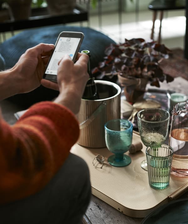 Une personne pianotant sur son téléphone devant une table basse remplie de verres.