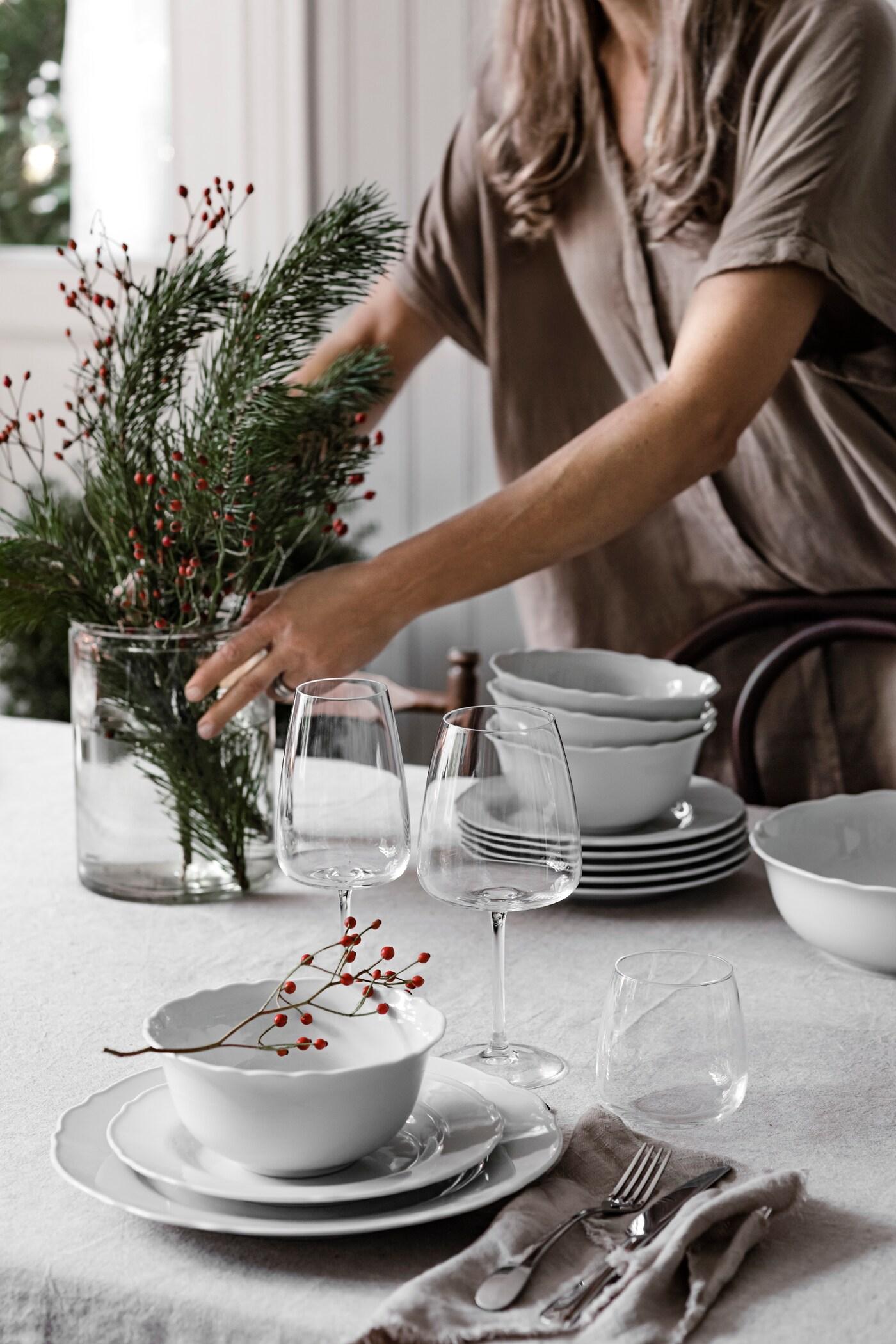 Une personne place un vase avec des branches de sapin sur une table de Noël de style campagnard.