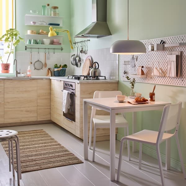 Une petite cuisine en beige, vert et blanc, une table MELLTORP et deux chaises empilables TEODORES, en blanc.