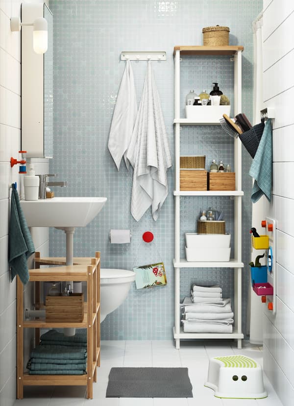 Une petite salle de bain familiale avec du carrelage blanc et bleu clair et une grande étagère blanche DYNAN ouverte offrant une vue sur des accessoires de salle de bain.