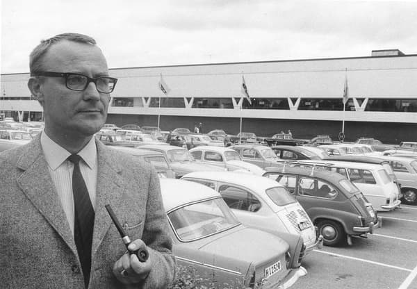 Une photo en noir et blanc du jeune Ingvar Kamprad fumant une pipe au milieu du parking extérieur d'un magasin IKEA.