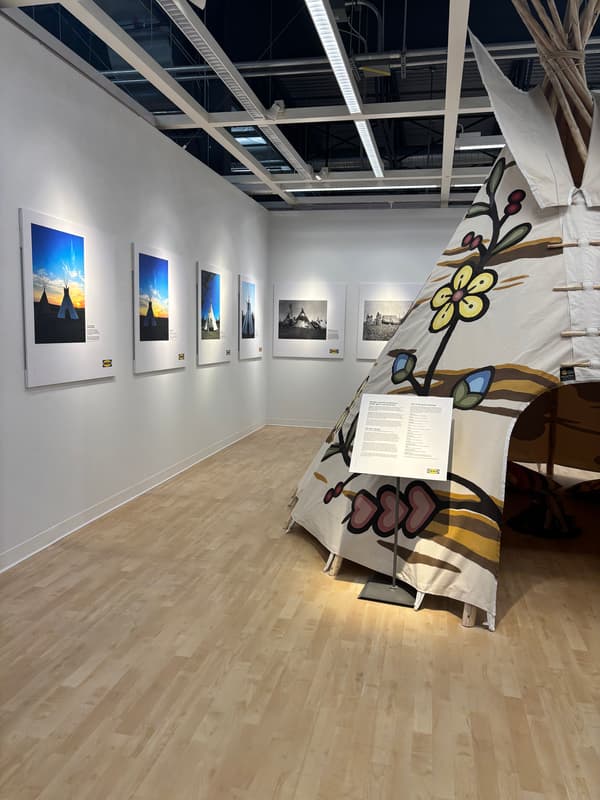 Une photo prise de loin d’un tipi installé dans un magasin, avec des photos accrochées à un mur blanc.