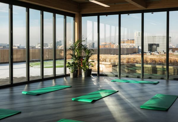Une pièce avec des tapis de yoga sur le sol et de grandes baies vitrées découvrant une vue sur la ville.