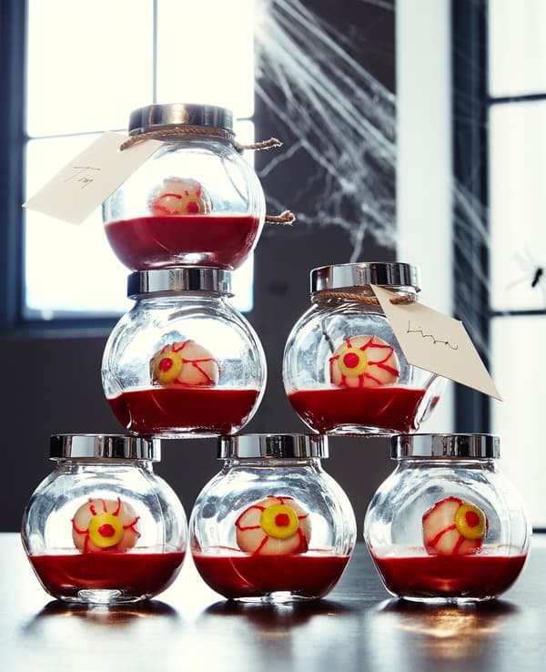Une pile de petits pots en verre remplis de gélatine rouge et de friandises qui ressemblent à des globes oculaires.