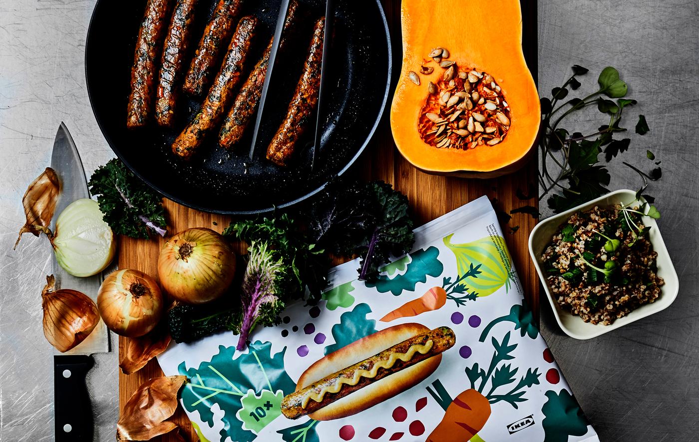 Une poêle remplie de saucisses, des légumes et un paquet de hot-dogs coloré sur une planche en bois.