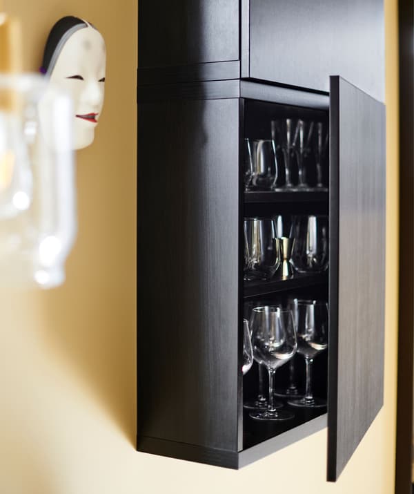 Une porte de l’armoire murale BESTÅ noire est ouverte pour laisser entrevoir des verres. 