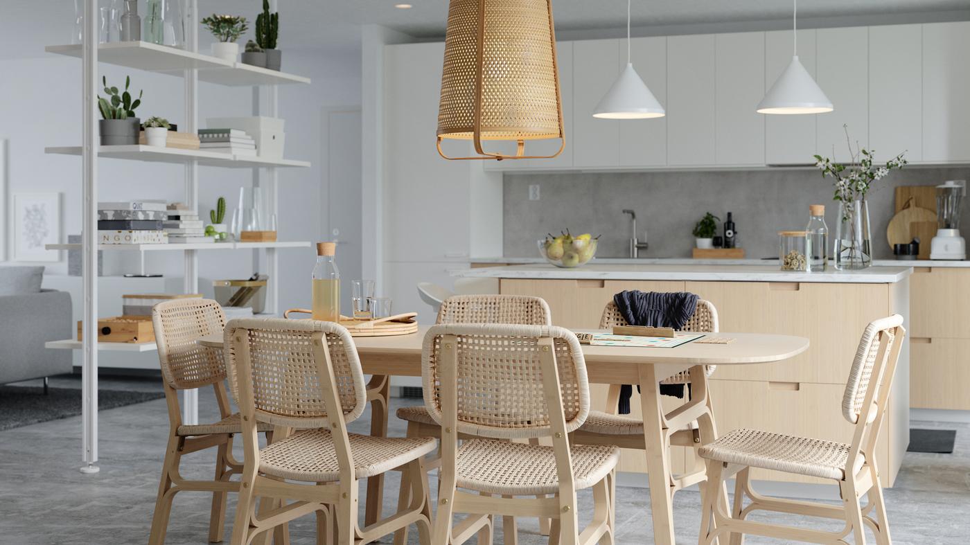Une salle à manger lumineuse avec une table et des chaises en bambou et papier tissé, un séparateur de pièces blanc et un îlot de cuisine.