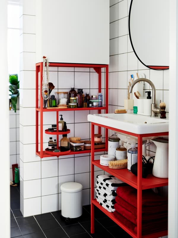 Une salle de bain carrelée de blanc meublée d’un mix de modules ENHET en rouge et blanc accueillant des objets décoratifs et des accessoires.