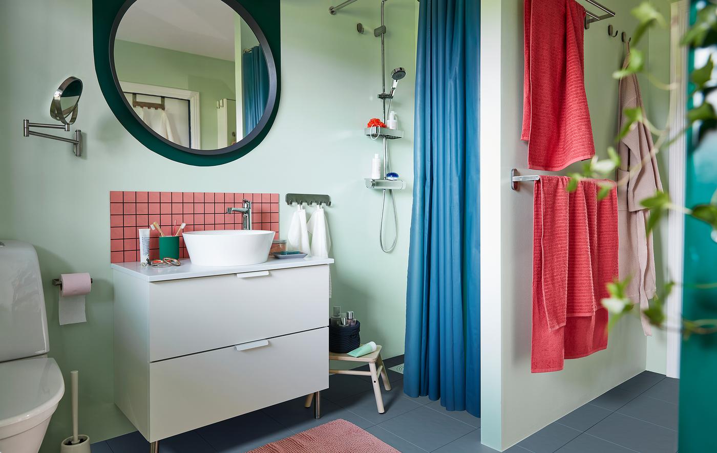 Une salle de bain complète bien organisée dans les tons pastel avec un lavabo, une douche, un porte-serviettes, un miroir, des plantes et des accessoires.