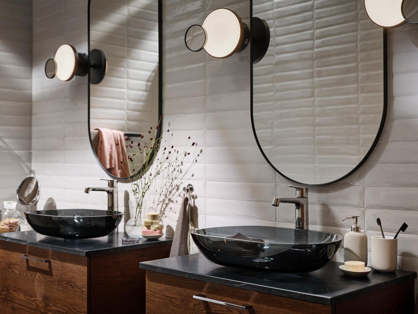 Une salle de bains avec deux vasques OXMYREN en verre gris foncé avec deux miroirs LINDBYN noirs au-dessus. 