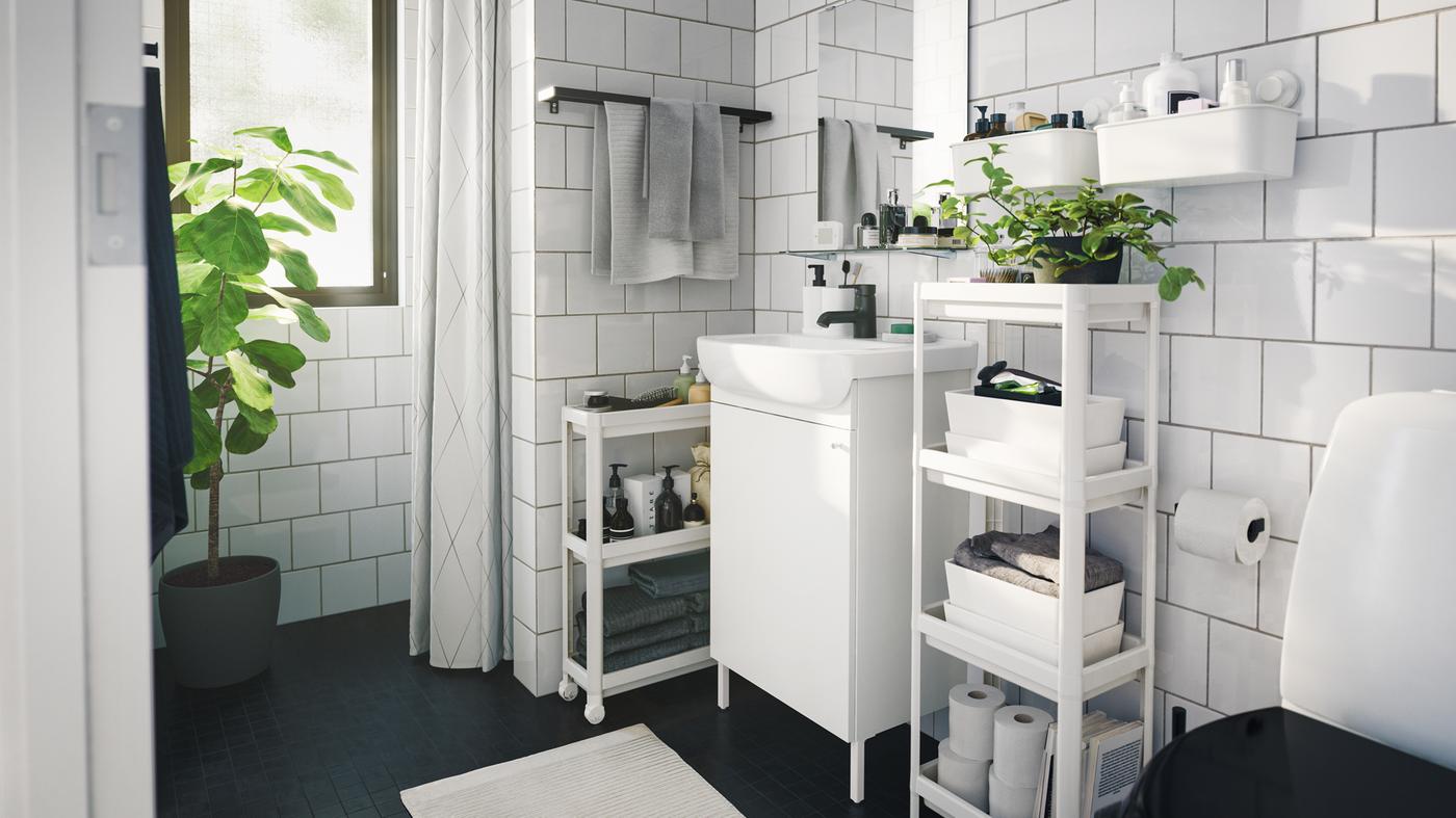 Une salle de bains contemporaine monochrome avec du rangement et des boîtes pour gagner de l'espace et des plantes vertes d'intérieur.