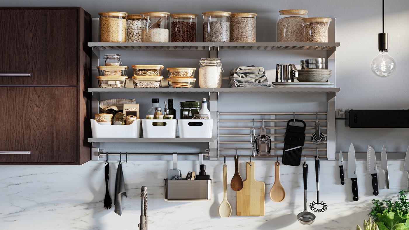 Une série de rangements de cuisine muraux KUNGSFORS avec des bocaux en verre avec couvercles, des boîtes de rangement VARIERA blanches et des ustensiles suspendus.