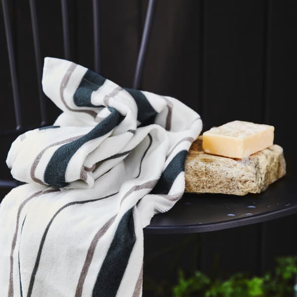 Une serviette blanche à rayures bleues et grises sur une chaise noire avec un pain de savon sur une pierre.