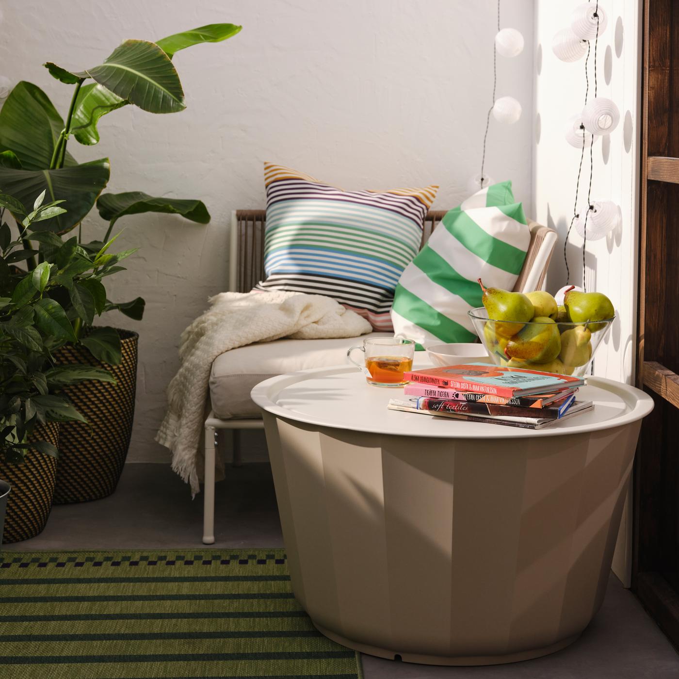 Une table basse LÅGASKÄR beige sur un tapis vert à rayures vert et violet et un module d'angle blanc et beige avec des coussins et un jeté.