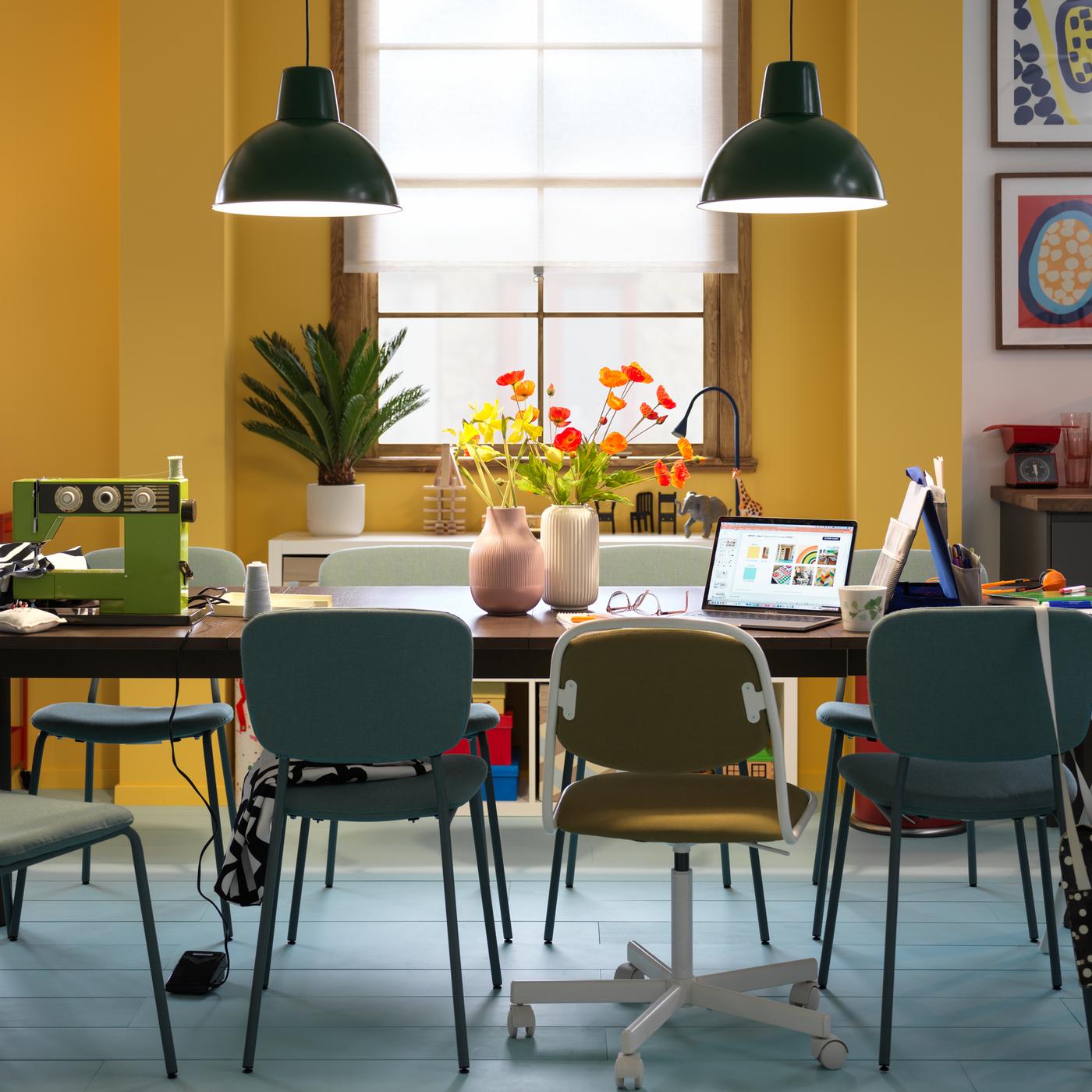 Une table extensible STRANDTORP brun foncé entourée de différentes chaises et divisée en différents postes de travail pour les activités de la journée.