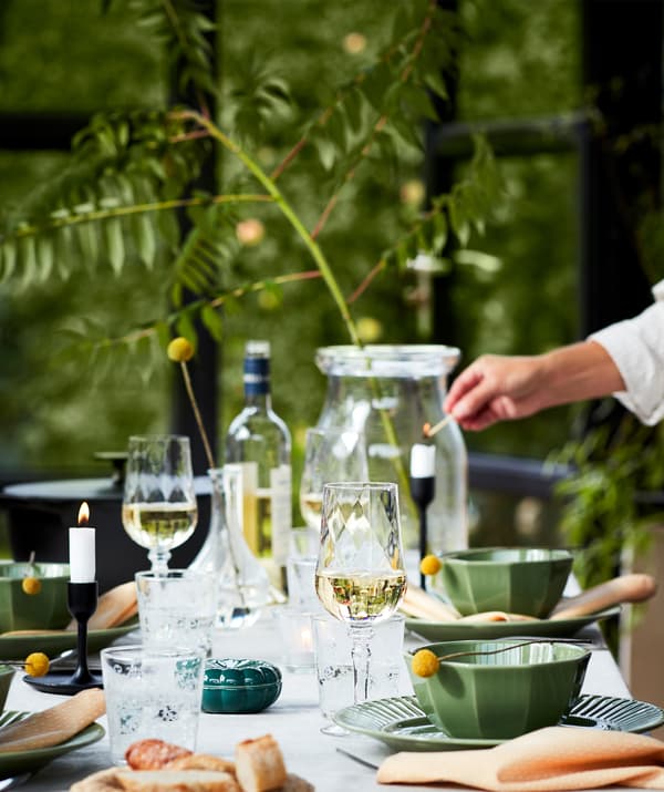 Une table joliment dressée pour un dîner en extérieur avec des assiettes vertes, des verres à vin, des bougies et bien plus. Avec naturel