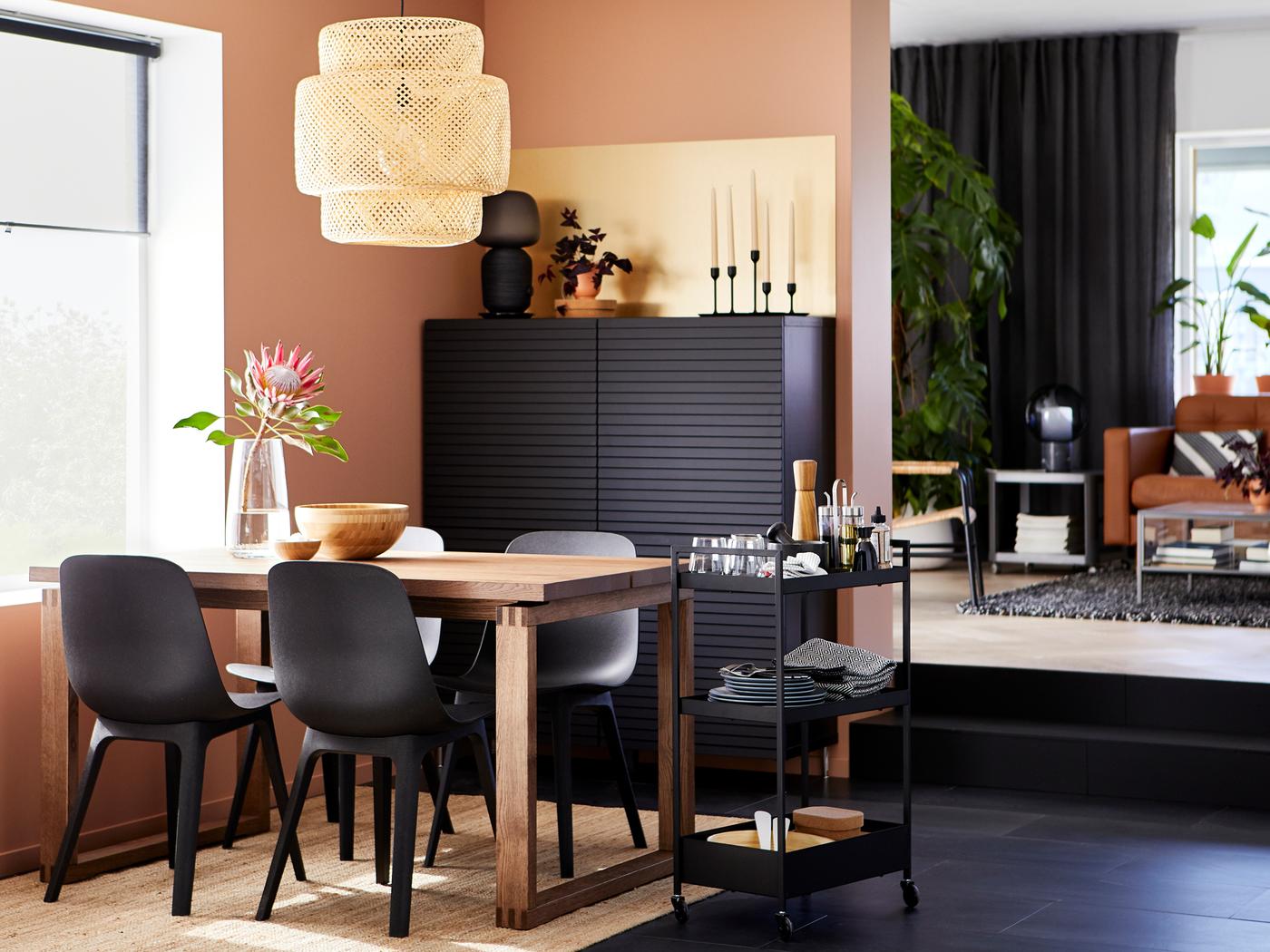 Une table MÖRBYLÅNGA en plaqué chêne brun et quatre chaises ODGER anthracite sont disposées près d’une desserte NISSAFORS.
